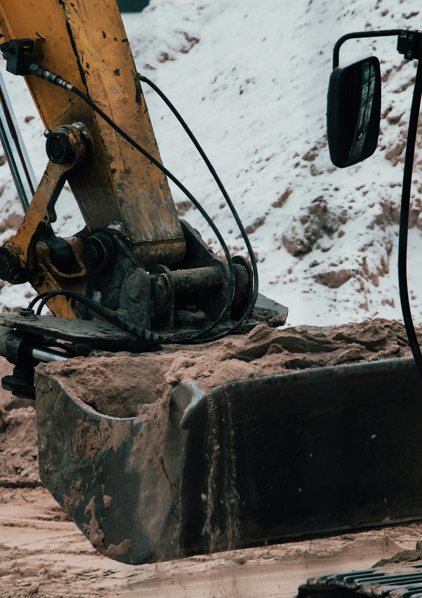 Close-up of an excavator shovel working on a snowy construction site, highlighting machinery details.