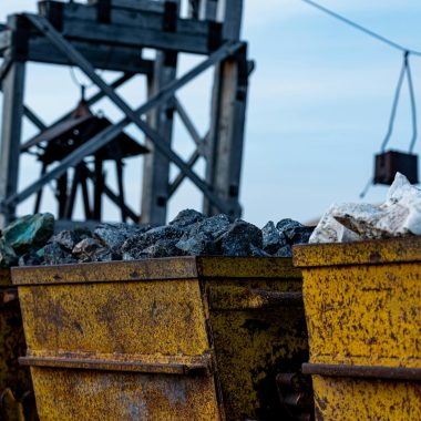 Detailed view of rusty mining equipment loaded with rocks under a clear sky.